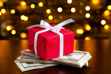Red gift box on the USA 100 dollar bills on blurred lights background. American dollar. Christmas and New Year money present. Gift cost. Hundred. Finance and business concept. Christmas shopping
