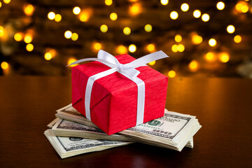 Red gift box on the USA 100 dollar bills on blurred lights background. American dollar. Christmas...