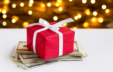 Red gift box on the USA 100 dollar bills on blurred lights background. American dollar. Christmas...