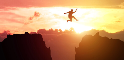 Obraz na płótnie Canvas Man jumping over precipice between two rocky mountains at sunset. Freedom, risk, challenge, success