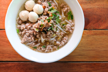 Top view of pork noodles clear soup with minced pork, pork balls and sprouts on the wooden table.