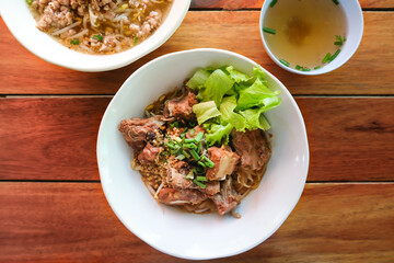 Top view of braised pork spare ribs noodles without soup, pork noodles clear soup and cup of clear soup on the wooden table.
