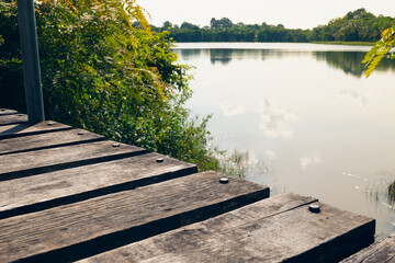 Close up view of rustic wooden bridge above the pond against reflection of sky and trees on calm water background.