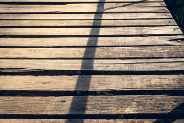 Texture of rustic wooden planks bridge against long shadow lines of fence.