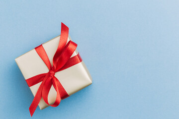 A single present wrapped in golden wrapping paper with a red ribbon bow sitting on a blue background