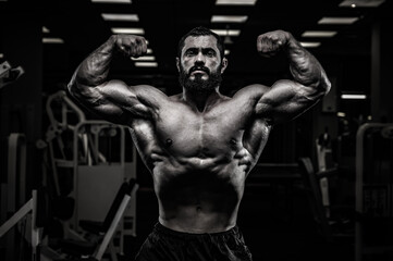 Fototapeta na wymiar black and white of strong young bearded athlete male showing double biceps pose in dark night sport gym