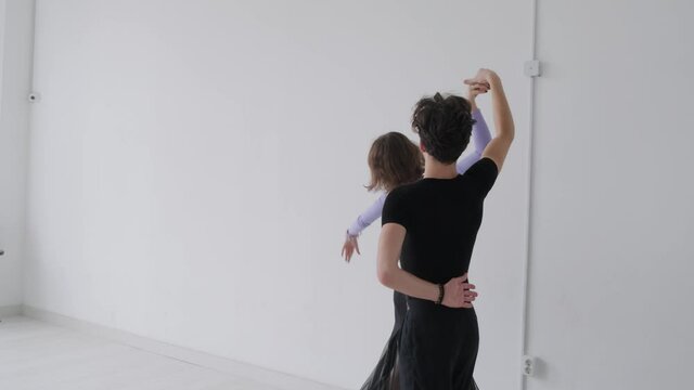 Young beautiful couple studying ballroom dance. A professional ballroom dancing couple dances in a large, bright, white hall