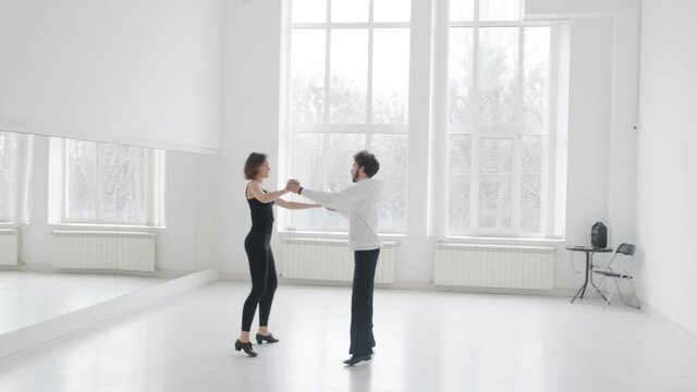 Young beautiful couple studying ballroom dance. A professional ballroom dancing couple dances in a large, bright, white hall