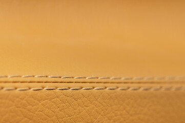 Close-up of beige orange faux leather stitching in the car interior. Background for interior trim comfort