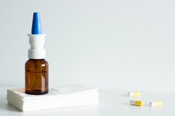 Nasal spray with blue cap and brown glass on white tissues, three pills on the side