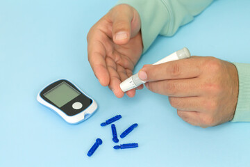 Man diabetic pricks finger by lancet pen and checks blood glucose level using glucometer