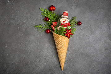 Snowman, thuja twigs and Christmas toys in a waffle cone. Dark gray background. An original sweet...