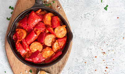 Sausages stewed with peppers, onions, and tomatoes in a pan on a gray concrete background. Copy space for text. Traditional Hungarian food lecho with sausages and vegetables.