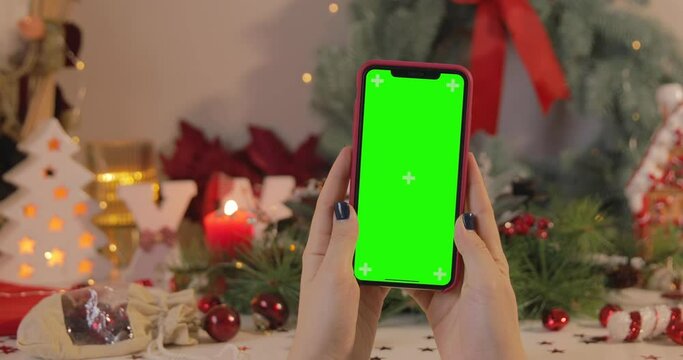 A woman Watching on iPhone 11 Pro Max with a green screen on a Christmas background. Horizontal orientation. POV. Keyed Chroma key.