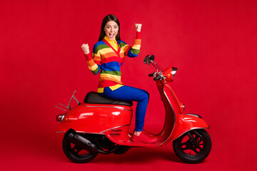 Obraz na płótnie Canvas Photo portrait of woman celebrating with two raised fists sitting on retro scooter isolated on vivid red colored background