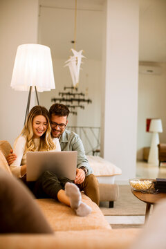 Young Couple Using Laptop Together While Sitting On Sofa At Home