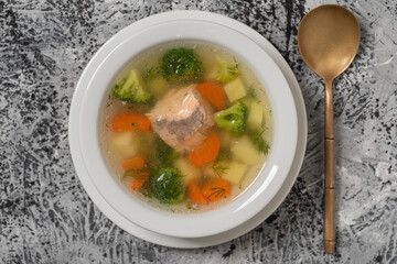 Fresh salmon fish soup with carrots, potatoes and onions in a white plate, close up. Top view