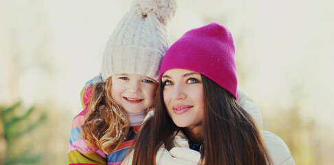 Portrait of happy smiling mother and little child wearing a colorful clothes in winter day over snowy background