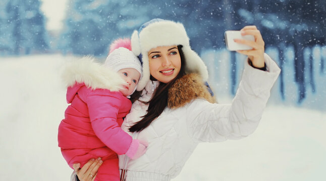 Portrait of happy smiling mother and little child taking selfie picture by smartphone in winter day over snowy background