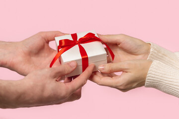 Man and Woman hands holding Gift box with red bow on pink background, close-up. pastel colors, copy space for text. Valentine gift. Banner for Christmas, hew year, birthday concept.