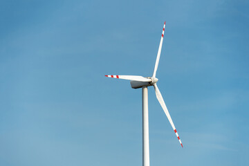 view of a modern windmill against a blue sky. The white blades of the wind turbine close up. Renewable energy source. Production of cheap and safe electricity.