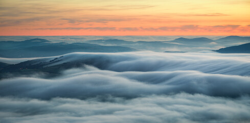 Wavy blankets of thick fog over valleys and hills