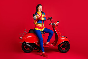Obraz na płótnie Canvas Photo portrait of winking girl paying via terminal with credit card sitting on scooter isolated on vivid red colored background