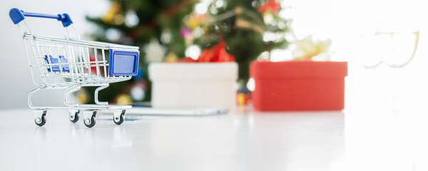 Online shopping concept. Shopping cart on white table with Christmas tree and decoration background.