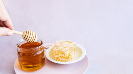 glass jar full of honey, plate with honeycomb on light brown background