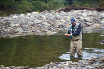 Smiling man walking in river and fishing with rob