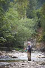 Mature man using rod for catching fish in mountain river