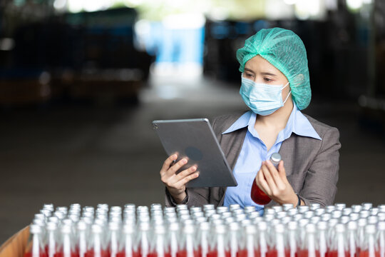 Young Woman Manager Wearing Safety Hat And Medical Mask For Protect Virus(covid-19) Using Tablet Computer For Stocktaking Of Products In Beverage Factory