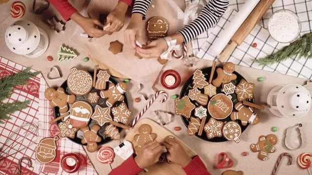 Kids is decorating a traditional gingerbread. Xmas flat lay video. Christmas and New Year holidays mood. Three children glaze a cookie. Top view of home table.