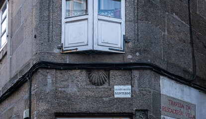 The scallop shell symbol of the Camino de Santiago and an insurance sign on a building, in the city of Santiago de Compostela, Spain
