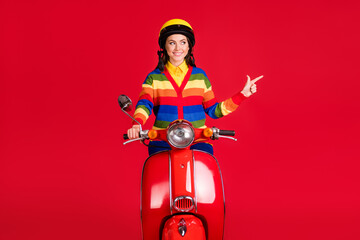 Photo portrait of woman pointing finger looking to side driving scooter isolated on vivid red colored background