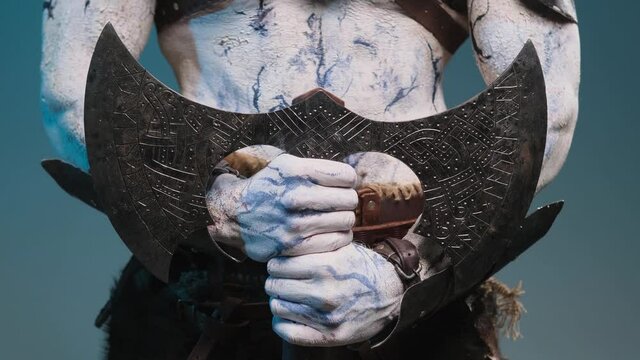 Iced and evil northern dead warrior holding steel two handed double axe with pale arms with naked torso in dark blue background.