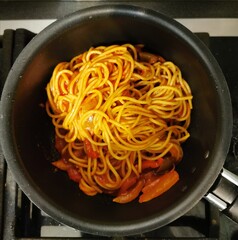 Italian pasta with tomatoes and paprika in a teflon black frying pan with a handle