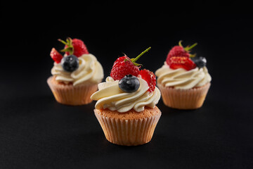 Tasty cupcakes with berries and cream, isolated on black.
