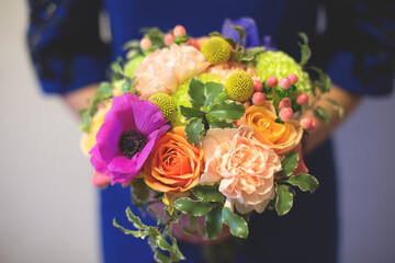 Close up of colorful bouquet in hands of florist in blue dress. Brightful and fresh mixed flowers bouquet with garden roses, carnations, anemones and greenery
