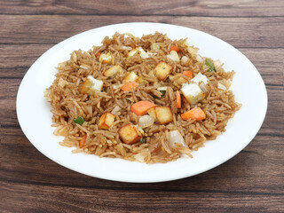 Healthy and tasty Paneer fried rice made of rice, mixed veggies and paneer, served in bowl over a rustic wooden background, Indo chinese, Indian cuisine, selective focus