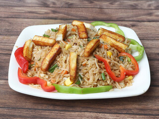 Healthy and tasty Paneer fried rice made of rice, mixed veggies and paneer, served in bowl over a rustic wooden background, Indo chinese, Indian cuisine, selective focus