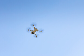 White unmanned aerial vehicle with four propellers and blades is in the blue sky background