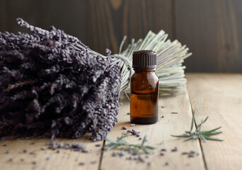 Lavender essential oil in the bottle with lavender bouquet and herb leaves nearby on rustic wooden...