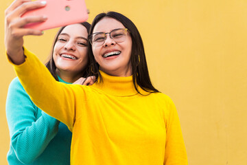 two pretty young smiling hispanic women in blue and yellow sweaters with braces on their teeth...