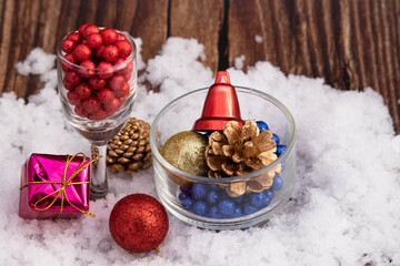Various Christmas Ornaments Glitter Balls Conifer Pine Cone And Maroon Red Bell In Wine Glass And Crystal Bowl On White Snow Over Brown Textured Wooden Background