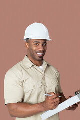 Portrait of happy young African male construction worker holding clipboard over brown background