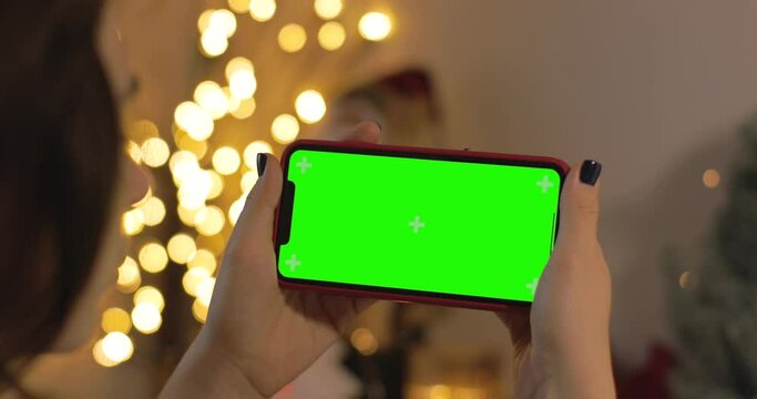 Back view of woman holding iPhone. green screen. Woman talking, smiling, laughing in a video calling with her family during Christmas time. Christmas quarantine at home.