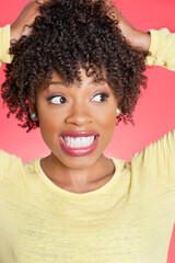 African American looking sideways with hands in hair over colored background