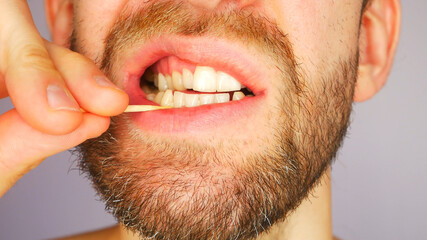 A young man takes out the remnants of food stuck in his teeth with a toothpick close-up