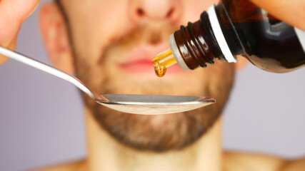 A young man pours medicated syrup into a teaspoon close-up